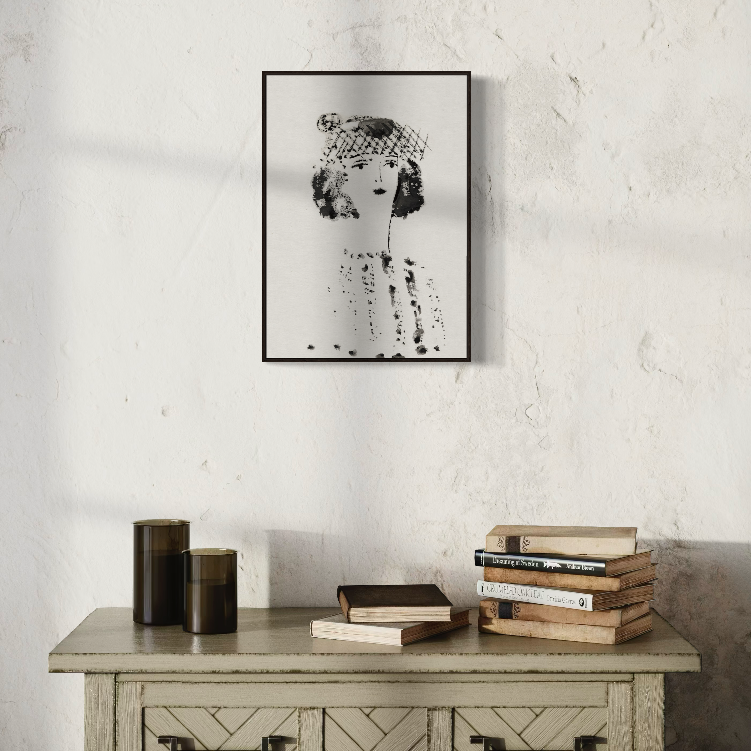 Framed black and white portrait of a young woman art print on a textured wall above a wooden cabinet with books.