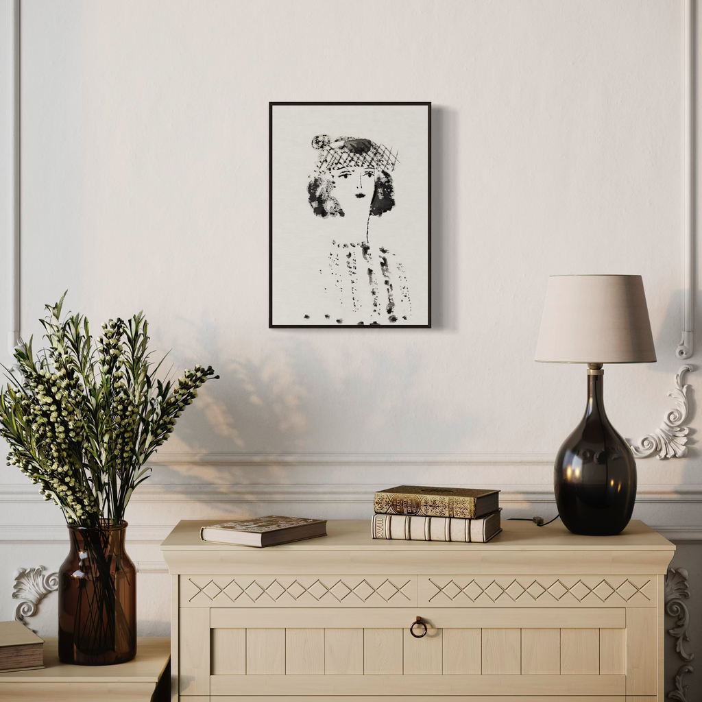 Decorative interior scene with a framed black and white portrait art print, lamp, and books on a wooden cabinet.